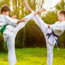 An Image of Two Boys Training Martial Arts Against Outdoor Background.