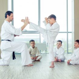 A Karate Trainer teaching a young kid how to kick the opponent.