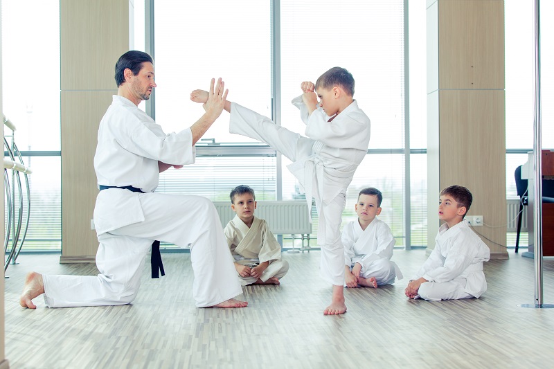 A Karate Trainer teaching a young kid how to kick the opponent.